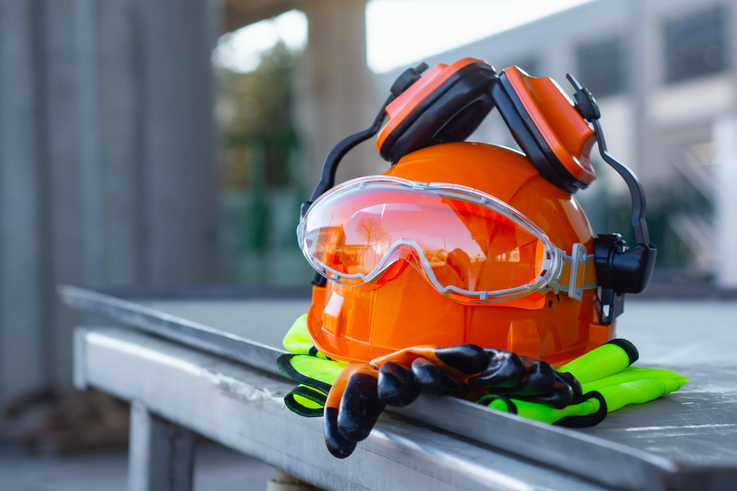 Construction safety helmet with protective goggles, gloves and reflective vest on industrial site.